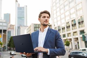 Picture of a serious handsome young business man standing near business center using laptop computer.; Shutterstock ID 1445094773; purchase_order: -; job: -; client: -; other: -